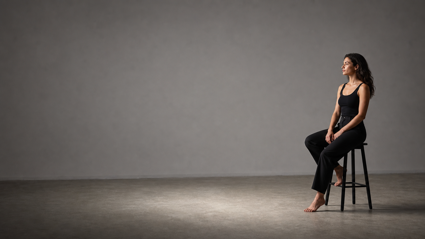 Studio portrait subject seated on a stool in a gray studio.